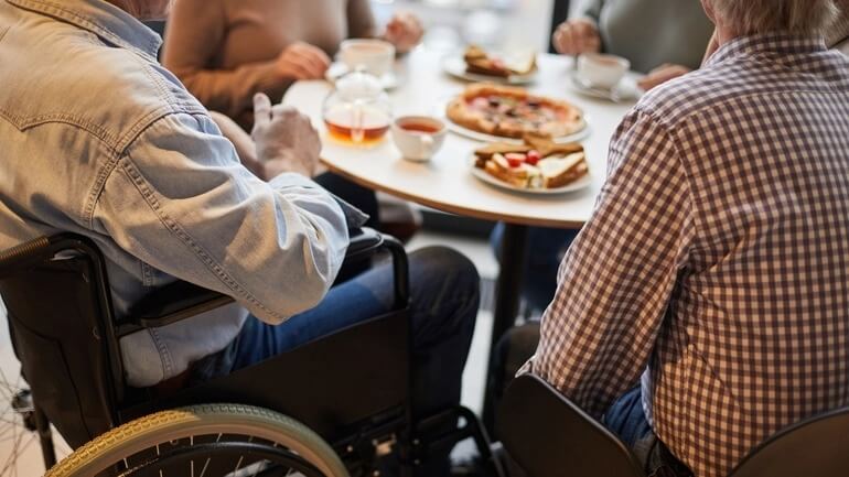 A person sitting in a wheelchairs at a restaurant table topped with food and drinks.