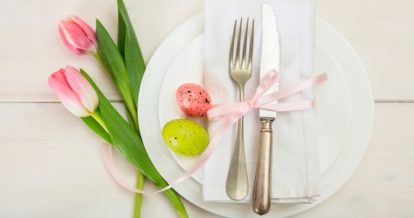 restaurant plate and cutlery decorated for Easter with pink flowers, eggs, and a ribbon.