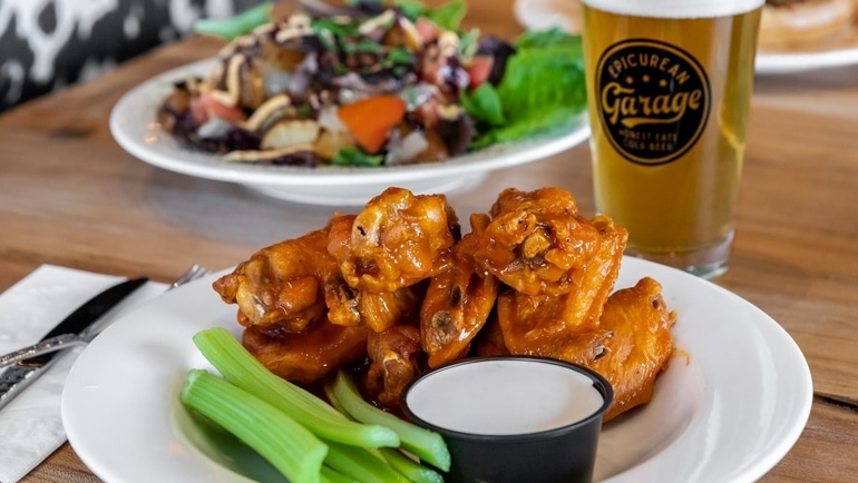 A plate of wings and a beer glass stamped with the logo of Epicurean Garage.