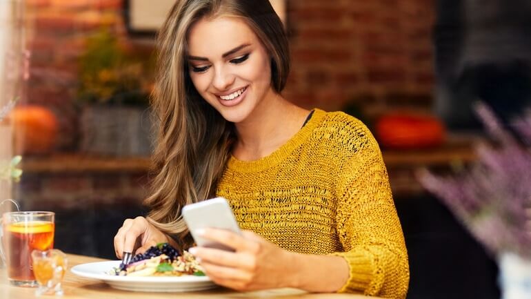 Young woman looking at phone while sitting and eating in a cafe