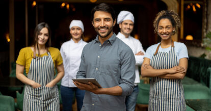 Five restaurant staff standing in front of a restaurant smiling.
