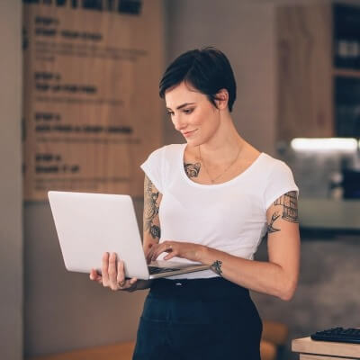 Female restaurant worker holding an laptop while typing.
