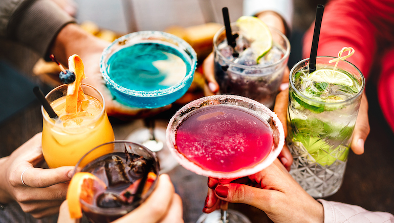 People hands toasting multicolored fancy drinks - Young friends having fun together drinking cocktails at happy hour - Social gathering party time concept on warm vivid filter