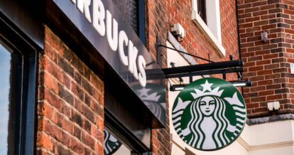 A Starbucks coffee sign handing outside of a red brick building.
